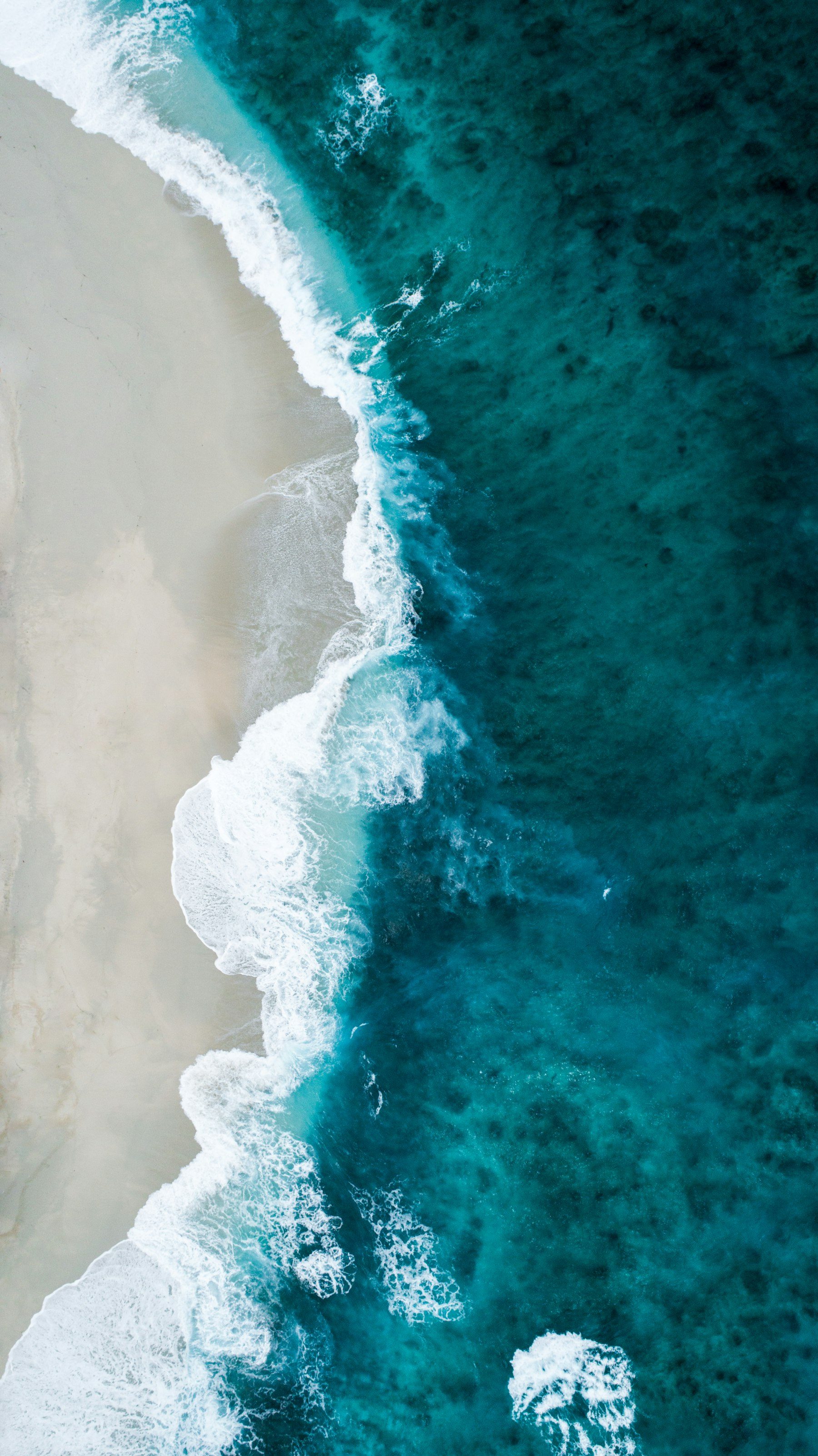 Aerial view of turquoise ocean waves breaking onto a pale sand beach