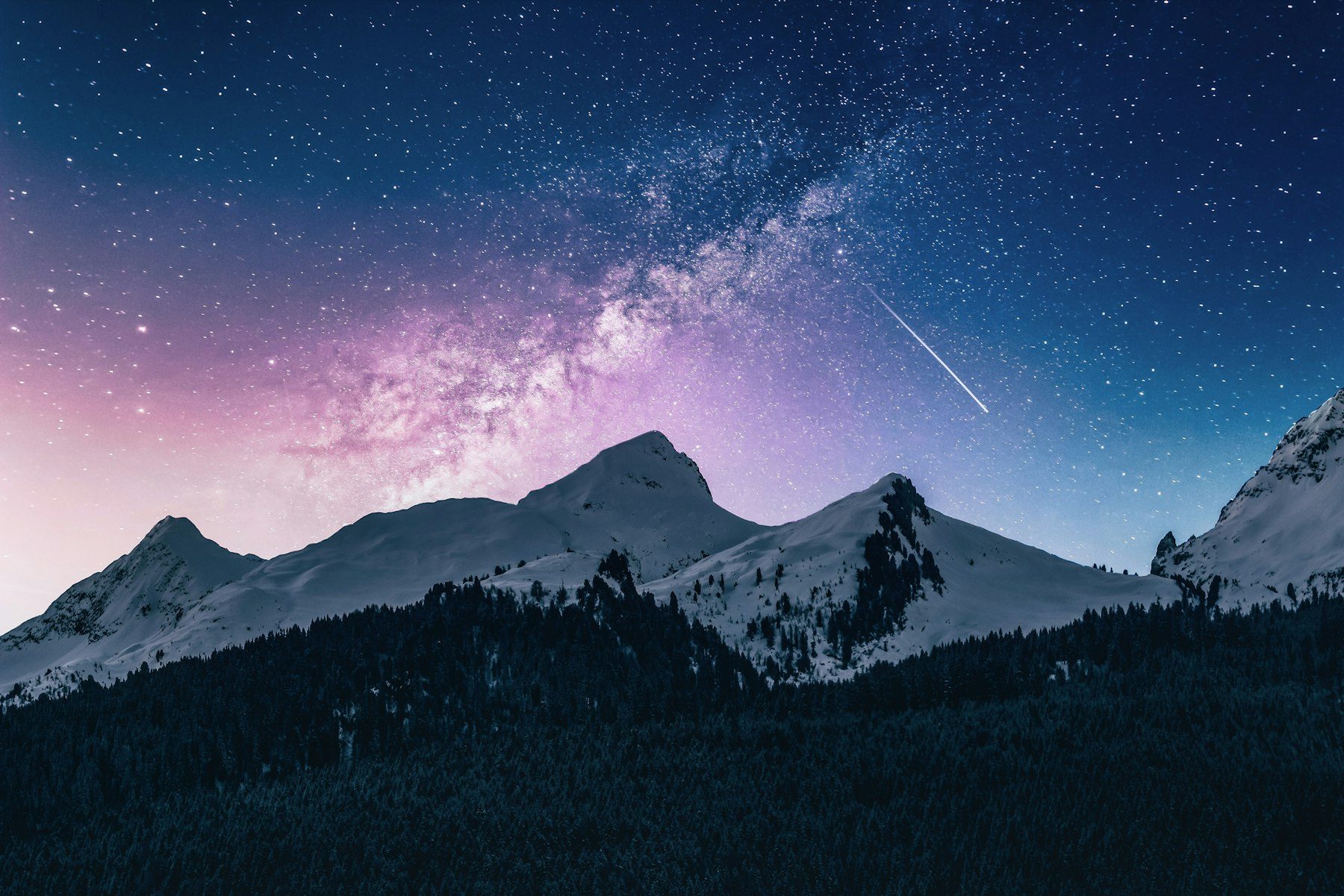 A shooting star crosses the Milky Way above snow-covered peaks at night