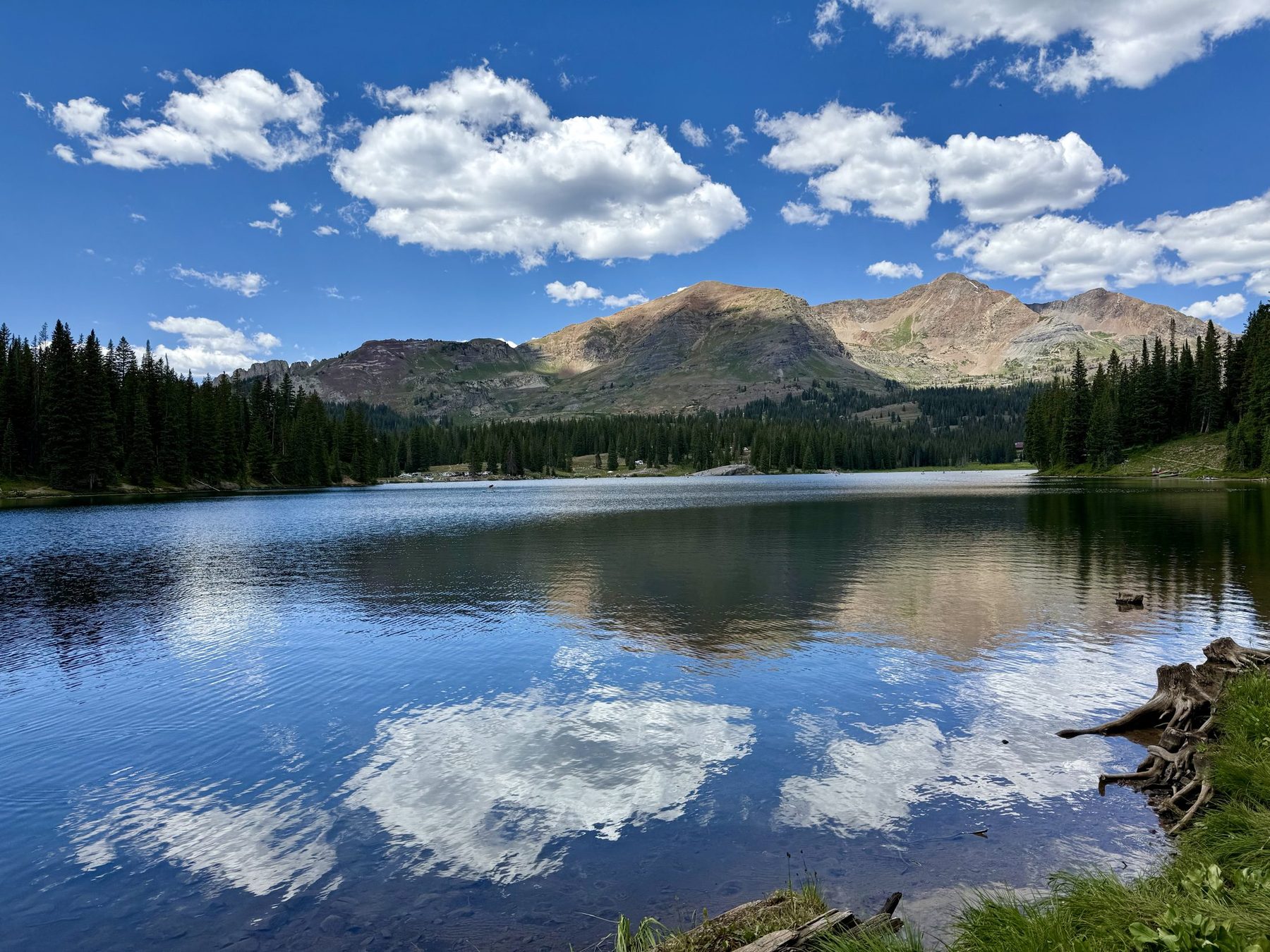 A still alpine lake mirrors mountain peaks and clouds under a blue sky